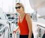 A woman in sunglasses stands on a yacht, enjoying a sunny day outdoors.